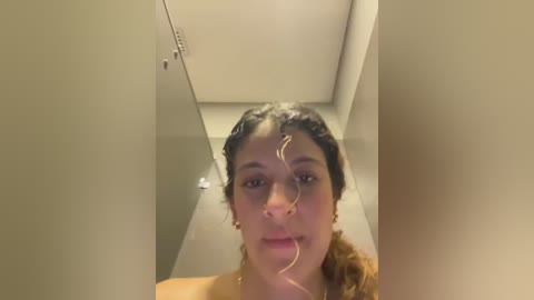 Media: Video of a young woman with curly brown hair, wearing a nose ring, and a clear tube attached to her nose, in a beige-walled hallway.