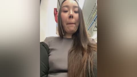 Media: Video of a young woman with long brown hair, wearing a grey shirt and headphones, sitting on a bus. Background includes other passengers and bus interior.