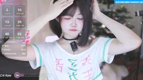 Media: A video of a young East Asian woman with fair skin and short black hair, wearing a white T-shirt with pink kanji, adjusting her hair, indoors, with a live-streaming overlay.