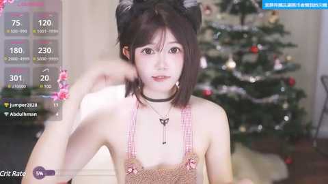 Media: A young Asian woman with fair skin, wearing a pink crochet top and black choker, poses in front of a decorated Christmas tree.