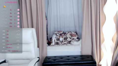 Media: Video of a modern bedroom with beige curtains, white chair, wavy sheer curtains, and a bed with brown and white floral comforter.