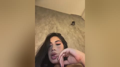 Media: A video of a Latina woman with long black hair and light skin, wearing heavy makeup, lying on a beige carpet, with a black shoe nearby.