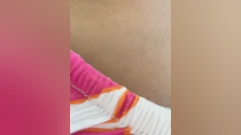 Media: A close-up video of a person's upper arm, featuring light brown skin and a pink sleeve with orange accents. The image is blurry, focusing primarily on the texture of the skin and clothing.