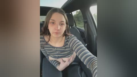 Media: A video of a young woman with fair skin and shoulder-length brown hair, wearing a striped top, sitting in a car with a neutral expression.