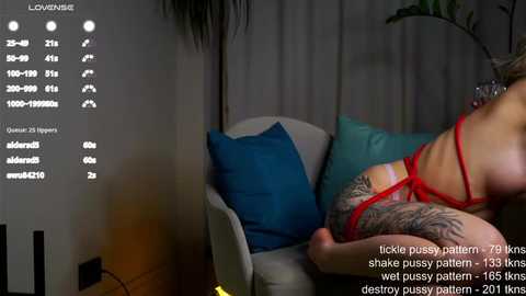 Media: Video of a woman in red lingerie, lying on a teal cushioned chair, with a large tattoo on her thigh. Text overlay mentions 'tickle pussy pattern'.