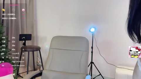 Media: Video of a modern living room setup with a beige recliner, a tall light stand with a glowing blue bulb, and a small black stool. Background includes a white wall, curtains, and a pink and white toy.