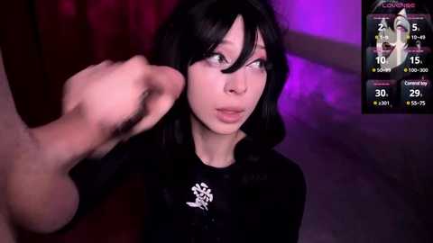 A video depicts a young woman with shoulder-length black hair, light skin, and wide eyes, being grabbed forcefully by a hand. She wears a black top with a white emblem. Background: purple and red lights.