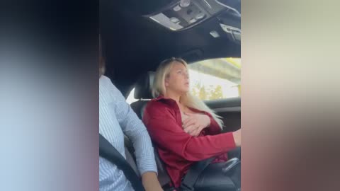 Media: Video of a blonde woman in a red shirt, wearing sunglasses, leaning back in a car seat, with a man partially visible on the left.