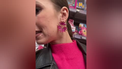 Media: A video of a young woman with light skin, brown hair, and a bright pink sweater. She wears large, ornate, purple earrings. Background includes toy store shelves and colorful packaging.