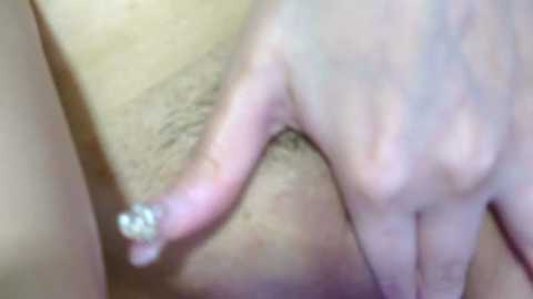 Media: A close-up video of a hand with a tattoo and a small, clear rhinestone nail, resting on a person's skin with visible hair. The image is slightly blurry.