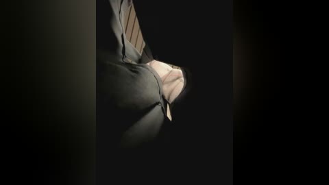 Media: A video of a person's right hand, wearing a light gray dress shirt with a diagonal striped tie, against a dark, shadowy background. The image highlights the texture of the fabric and the contrast between light and shadow.