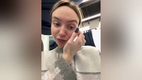 Media: A video of a light-skinned woman with brown hair, wearing a grey and white striped sweater, applying eyeliner while seated in a car, with blurred background.