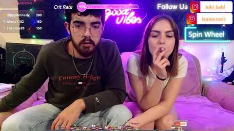 Media: Video of a young couple playing video games on a bed, set in a dimly lit room with neon lights and social media icons.