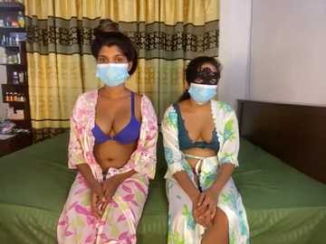 Media: Video of two South Asian women in blue face masks, wearing colorful patterned robes and matching bras, sitting on a green bed with yellow curtains.