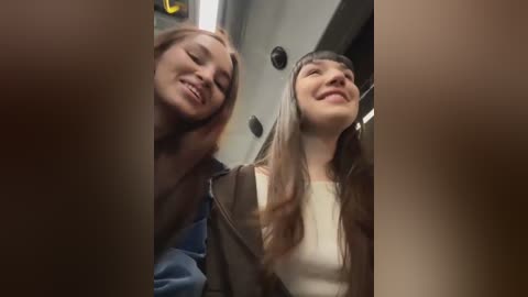 Media: A video captures two young women, one with long brown hair, the other with short blonde hair, smiling in a subway car, looking upward.