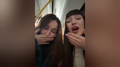 Media: Video of two young women, one with long brown hair, the other with short black hair, laughing and covering their mouths in a subway car.