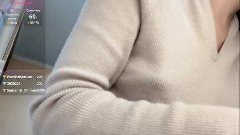 Media: Video of a close-up of a person wearing a beige, long-sleeved, ribbed sweater, with overlaid text displaying \"Feverish,\" \"Shivering,\" \"Chills,\" and \"Seizure\" symptoms, indicative of a medical assessment.