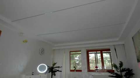 Media: Video of a bright, minimalist room with white walls, a ceiling fan, large windows, and a circular mirror. A red-framed clock hangs on the left wall.