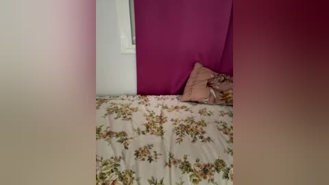 Media: Video of a small, cozy bedroom with a floral-patterned bedspread, a pink wall, and a white window with a curtain, creating a soft, feminine ambiance.