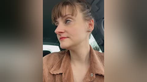 Media: A video of a woman with light skin and light brown hair in a bun, wearing a beige ribbed sweater, seen from the side in a car, looking thoughtful.