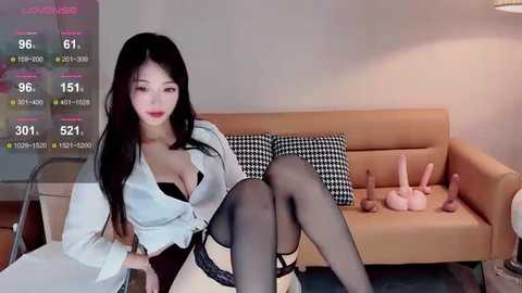 Media: Video of an East Asian woman with long black hair, wearing a white blouse, black lace bra, garter belt, and black stockings, posing on a beige couch.