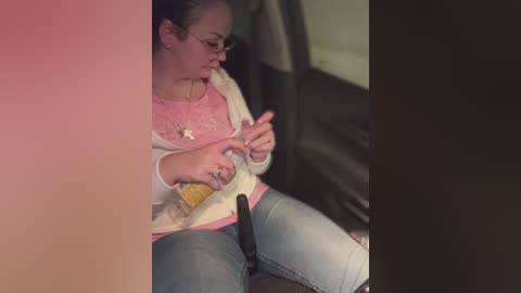 Media: A video of a woman in a car, wearing glasses, a pink sweater, and light jeans, adjusting her seatbelt. The background shows the car's interior.