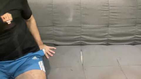 Media: Video of a person in a black t-shirt and blue athletic shorts standing on a gray padded mat with a black outline on the wall.