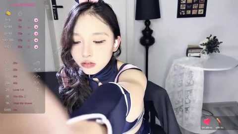 Media: A video of a young Asian woman in a blue dress, sitting with her eyes closed, in a modern, minimalist room with a round table and black lamp.