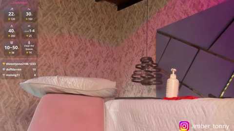 Media: Video of a modern, cozy room with a massage table, cushioned chair, and a beige, textured wall. A black, cone-shaped lamp hangs above the chair, and a lotion bottle sits on the table. The room is lit with warm, ambient lighting.