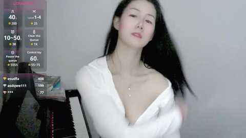 Media: A video of an Asian woman with long black hair, wearing a white off-shoulder top, sitting against a plain white wall, with a digital screen overlay displaying her stats and heart rate.