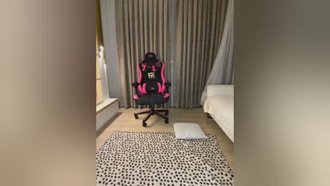 Media: A video of a modern gaming setup featuring a pink and black gaming chair, white bed, beige curtains, and a black-and-white patterned rug on a light wooden floor.