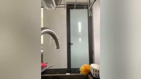 Media: Video of a modern bathroom with a frosted glass door, stainless steel sink, and white tile walls.