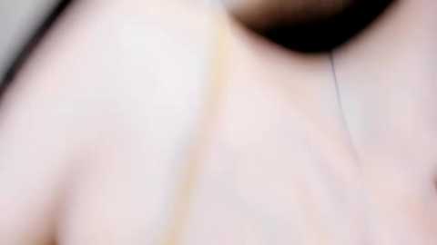 A close-up video of a light-skinned person's neck and upper chest, blurred and out of focus, featuring subtle skin texture and a faint gold necklace.