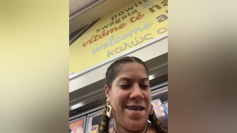 Media: Video of a smiling woman with braided hair, wearing large gold hoop earrings, inside a fast-food restaurant with a yellow sign and menu boards.