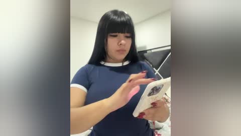 Media: A video shows a young woman with straight black hair, wearing a navy blue top, holding a book in a dimly lit room.