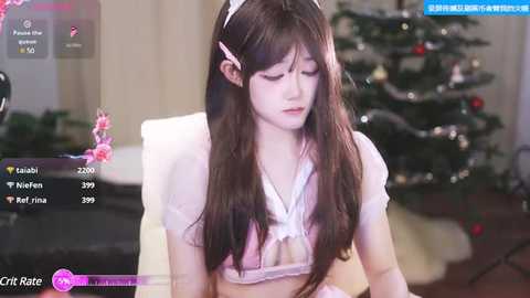 Media: A video shows a young Asian woman with long, straight black hair and a pink headband, wearing a revealing, white lace bra. She sits indoors, in a softly lit room with a Christmas tree.