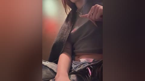 Media: Video of a woman with long brown hair, wearing a black leather jacket, denim shorts, and pink underwear, sitting in a dimly lit room with blurred background.