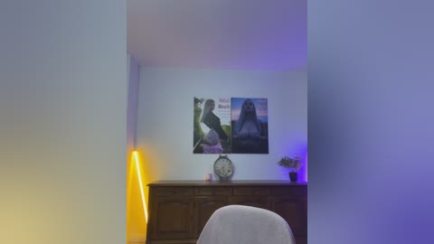 Media: Video of a minimalist room with a white wall featuring a large black-and-white poster of a woman and a clock. A tall, slim yellow lamp and a small plant sit on a wooden dresser.