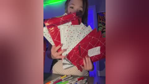 Media: Video of a woman with long brown hair, holding a stack of red and white gift wrap, surrounded by colorful pens on a desk.