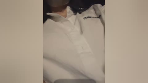 Media: A video showing a person lying on their back, partially obscured by a white blanket, wearing a white polo shirt with a logo on the right sleeve. The background is dark and indistinct.