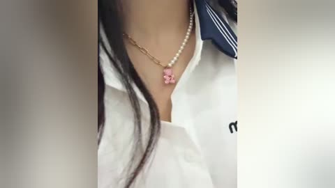 Media: A video of a woman's chest, wearing a white blouse with a blue sailor collar, a pearl necklace, and a pink pendant, long dark hair.