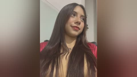 Media: Video of a Latina woman with long, straight, dark brown hair, wearing a red top, standing indoors with a blurred background.