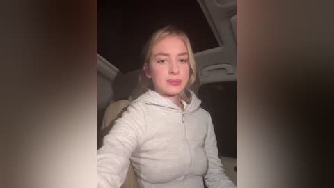 Media: A video of a blonde woman in a light gray hoodie, seated in a car at night with dim lighting. She has a neutral expression.