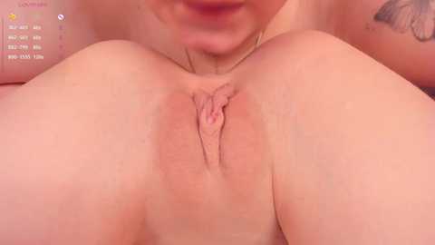 Media: Video of a close-up of a light-skinned woman's vulva, with her lips slightly open, and a tattoo visible on her arm. The background is blurred.