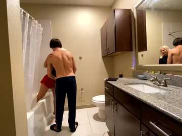 Media: Video of a shirtless man in red shorts and black socks standing in a bathroom, facing a naked woman in a bathtub, with a mirror reflecting his back.