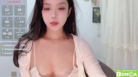 Media: Video of an East Asian woman with long black hair, light skin, and red lipstick, wearing a sheer lace bra and a light cardigan, in a well-lit room with a calendar and curtains in the background.