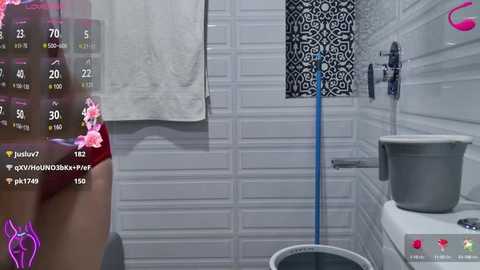 Media: A video of a modern, white-tiled bathroom with a white towel, a floral patterned shower curtain, and a toilet visible in the foreground. The image includes a digital overlay with chat messages.