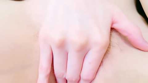 Media: A close-up video of a pale-skinned person's hand, fingers spread, resting on a soft, light-colored surface. The skin appears smooth with faint natural lines. The background is out of focus, highlighting the hand's details.