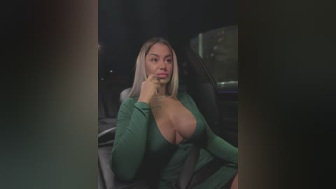 A video of a blonde woman with large breasts, wearing a low-cut green top, sitting in a car at night. She has a contemplative expression.