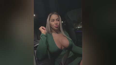 Media: Video of a curvy, light-skinned woman with long blonde hair and large breasts, wearing a deep green, plunging neckline dress, sitting in a dimly lit car.